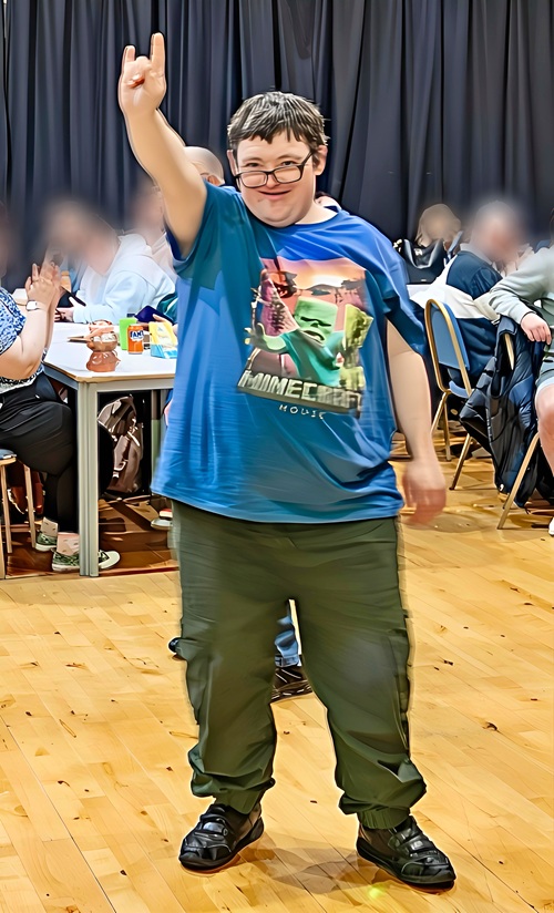 Man with short dark hair and glasses, wearing a blue Minecraft t-shirt and green trousers striking a pose!