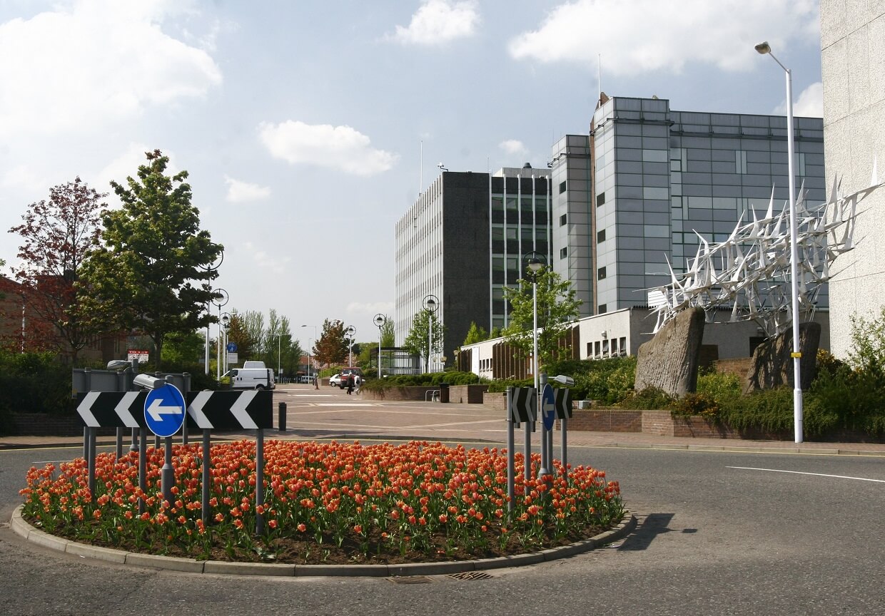 a view of Fife House building with several buildings, a roundabout with orange flowers, and street signs